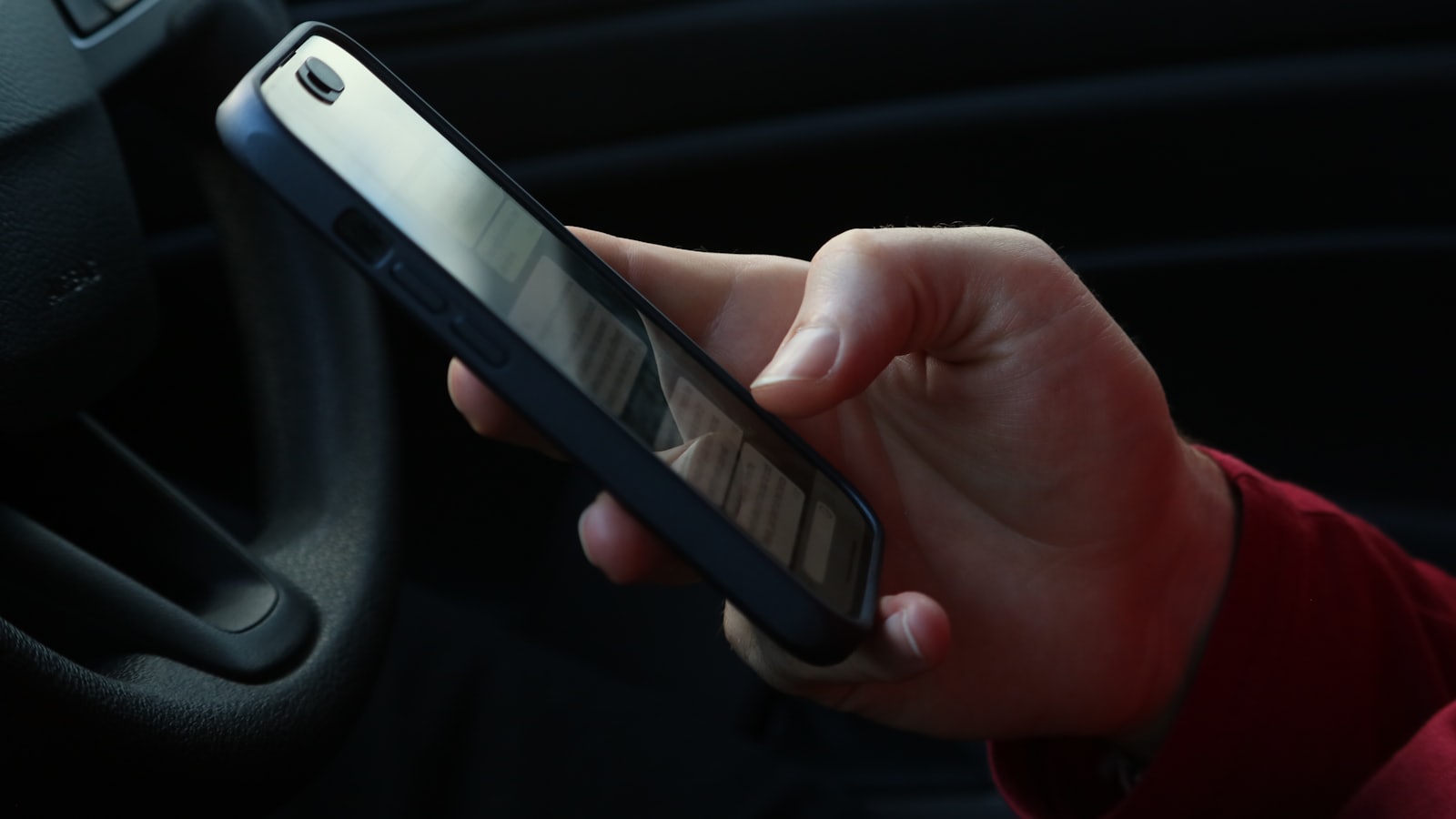 Kierowca trzymający smartfon z aplikacją w dłoni we wnętrzu samochodu